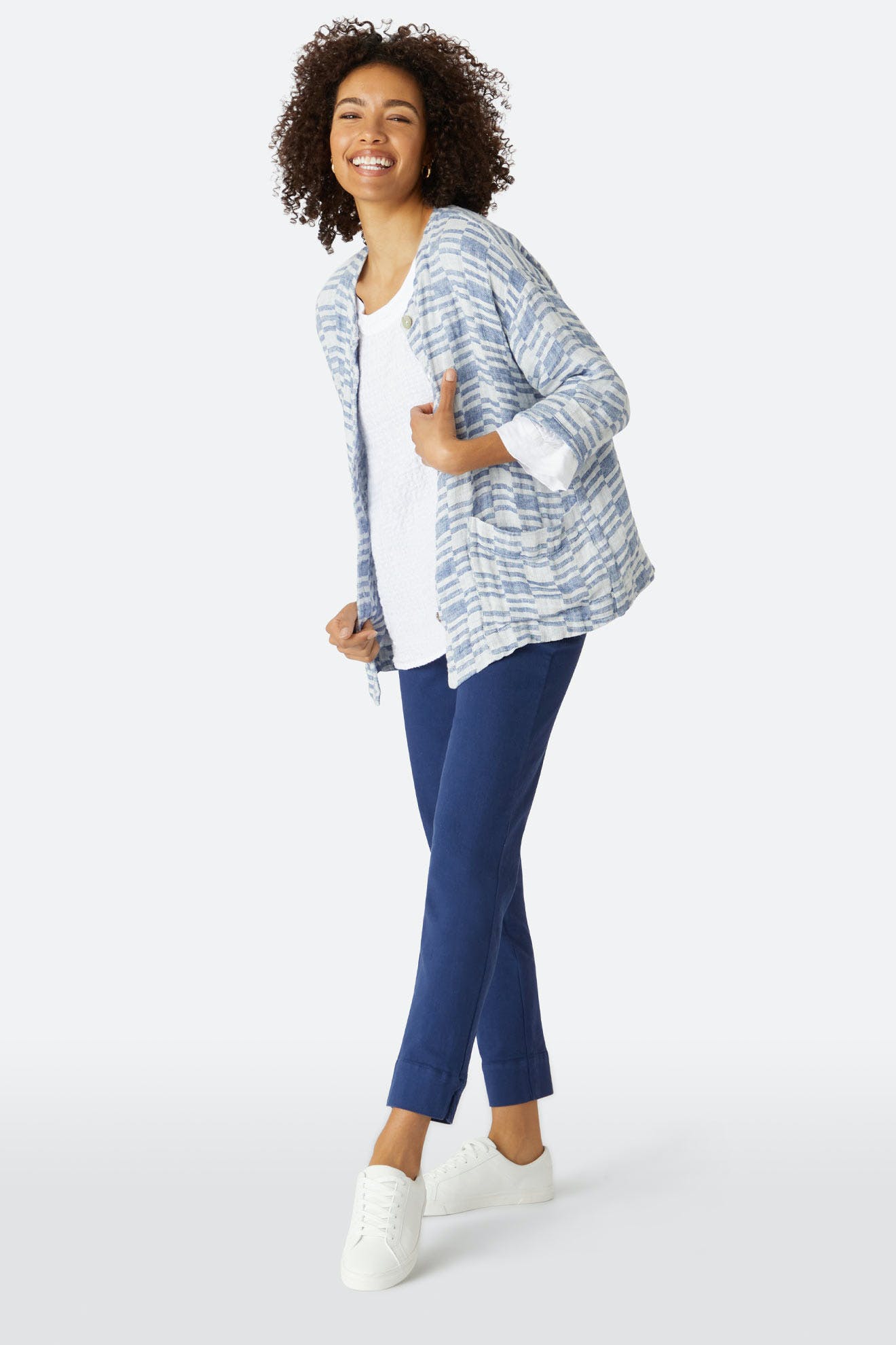 A woman smiles in a blue and white striped cropped jacket over a white top, paired with blue Stretch Cotton Twill Trousers and white sneakers, standing against a plain light background.