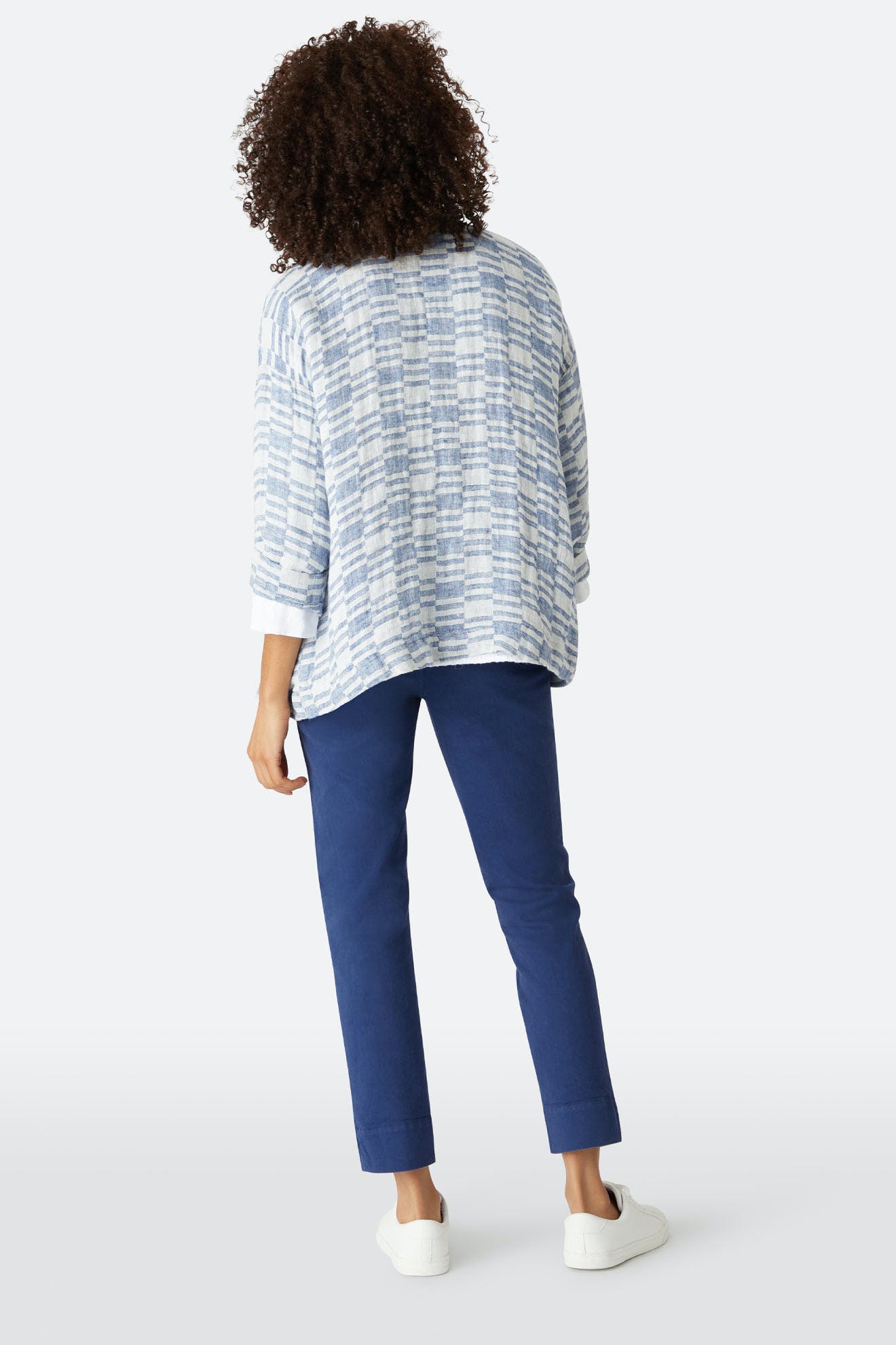 A person stands with their back to the camera, wearing a loose blue plaid top and Stretch Cotton Twill Trousers with an elasticated waist, paired with white sneakers, against a plain background.