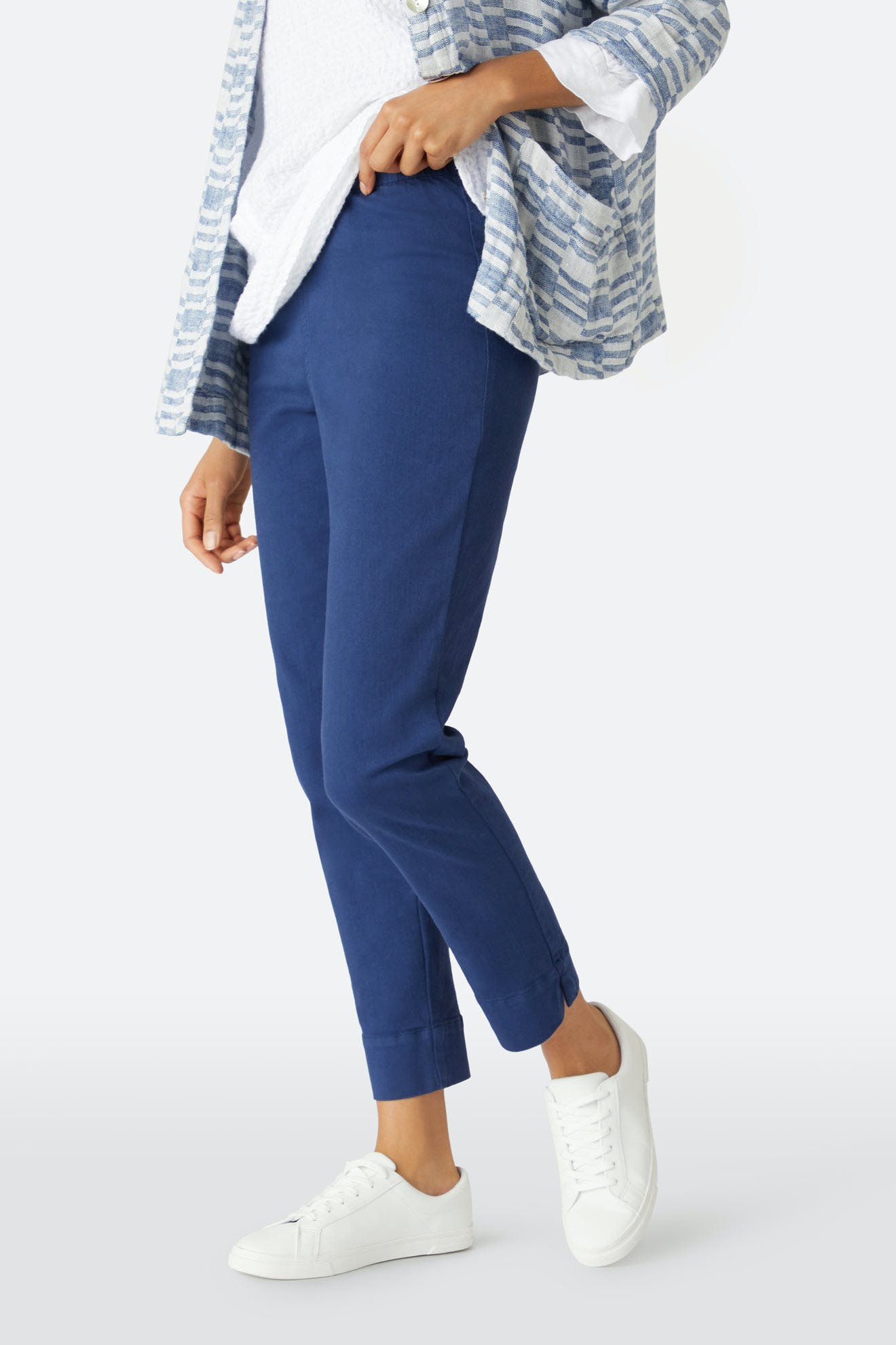 Person wearing blue Stretch Cotton Twill Trouser with an elasticated waist and cuffed hems, paired with a white top, blue-and-white striped cardigan, and white sneakers, standing against a plain background.