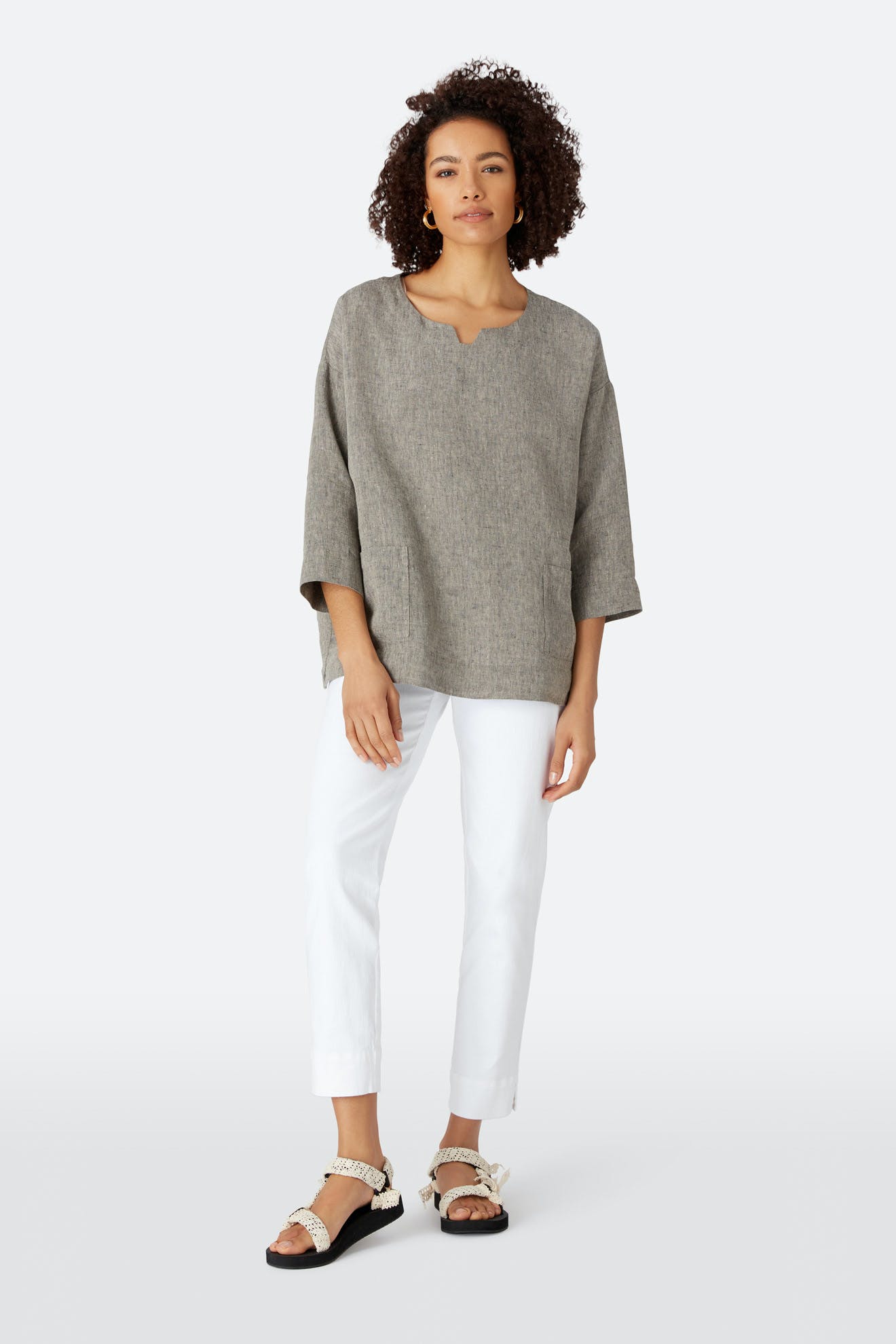 A person wears a loose grey top, Stretch Cotton Twill Trouser with slim, tapered legs and an elasticated waist, and black sandals with decorative straps, standing against a plain light background.