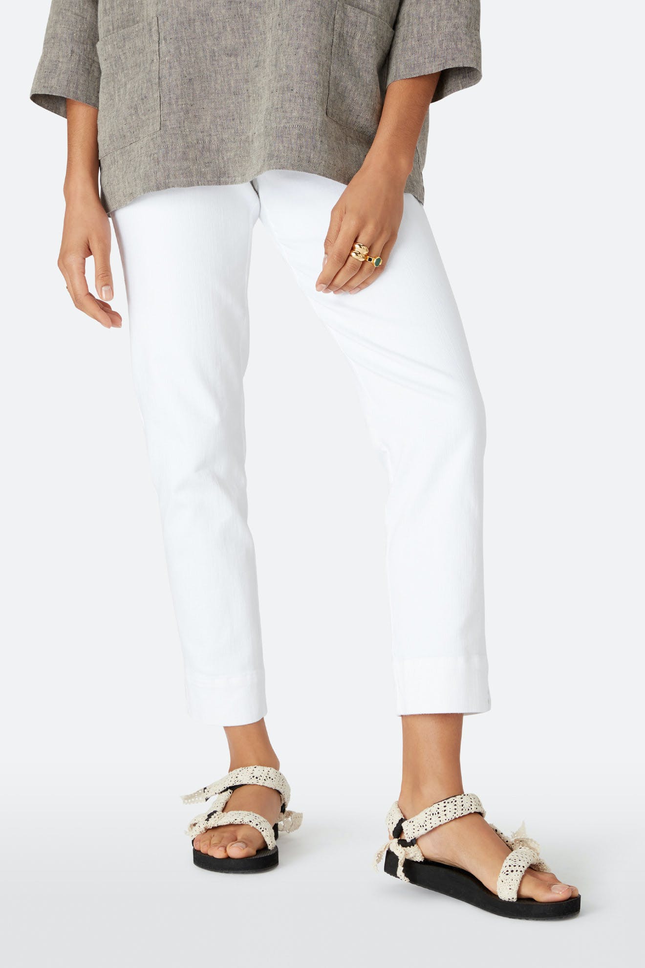 A person wears a grey long-sleeve top, cream textured-strap sandals, and white Stretch Cotton Twill Trousers while standing against a plain background.