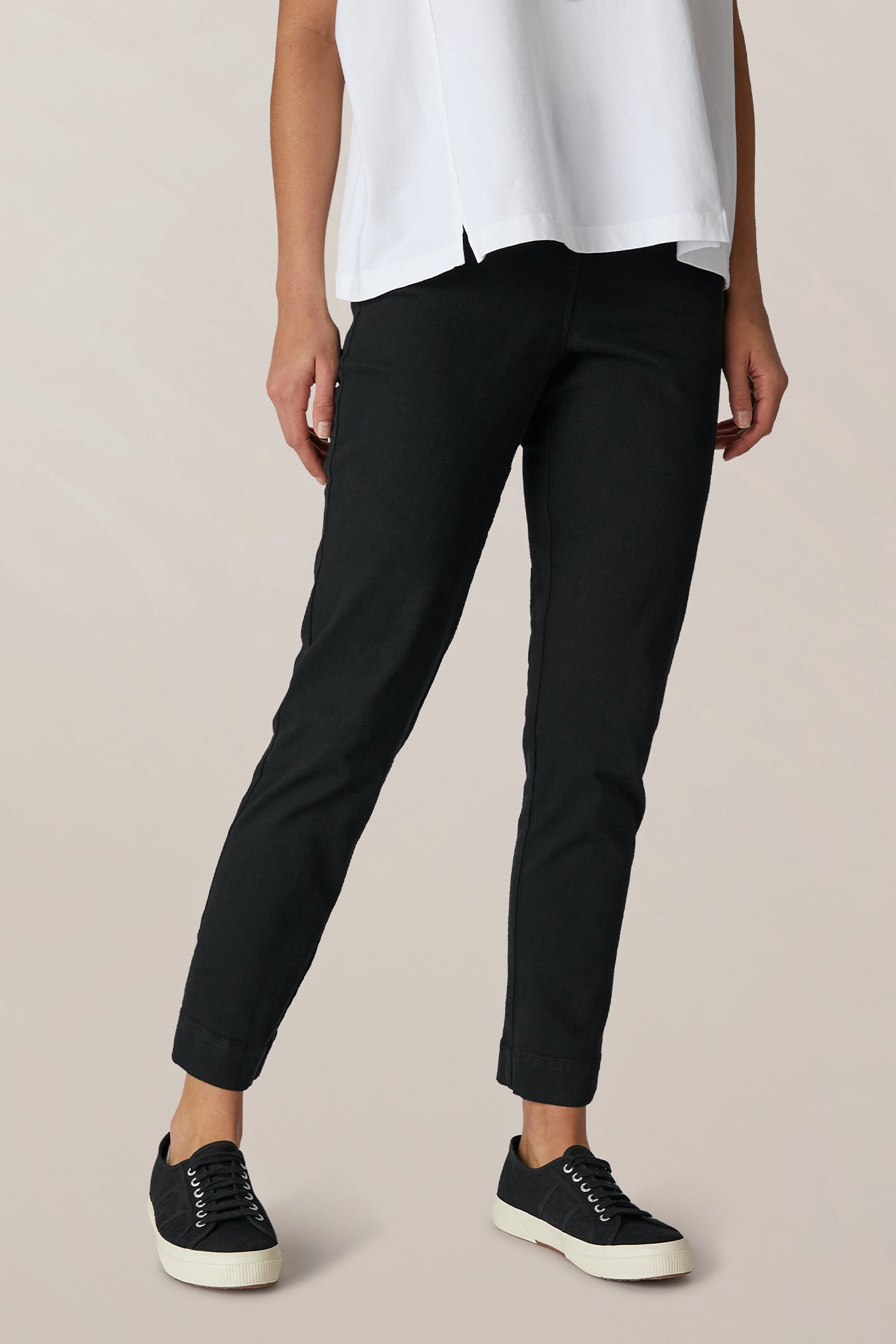 A person is wearing the SS22 Stretch Cotton Trouser with a white shirt and black sneakers with white soles, standing against a neutral background. Their face is not visible.