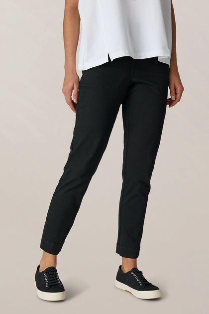 A person is wearing the SS22 Stretch Cotton Trouser with a white shirt and black sneakers with white soles, standing against a neutral background. Their face is not visible.