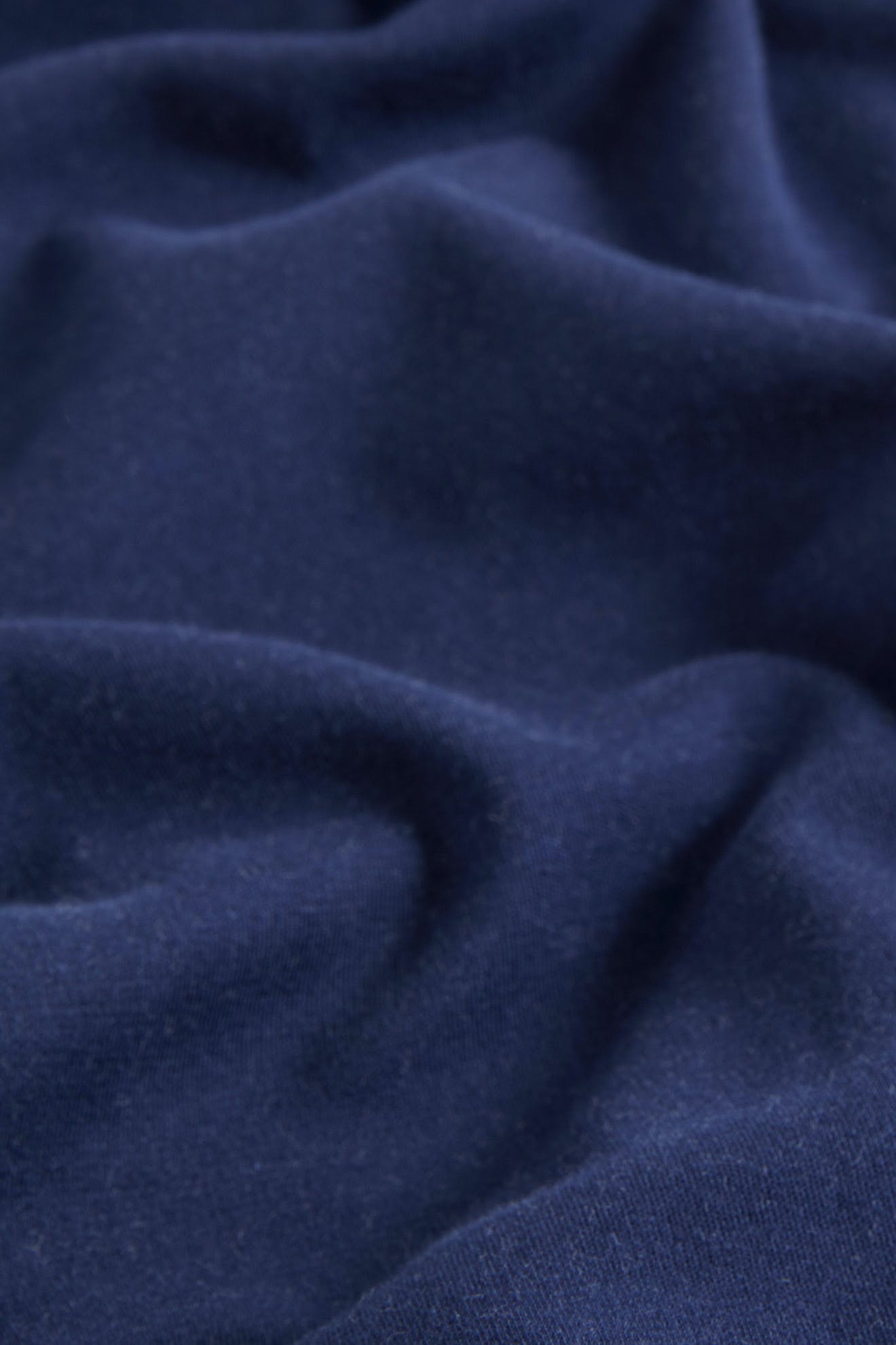 A close-up of the SS22 Stretch Cotton Trouser shows its dark blue OEKO-TEX cotton fabric with visible folds and texture.