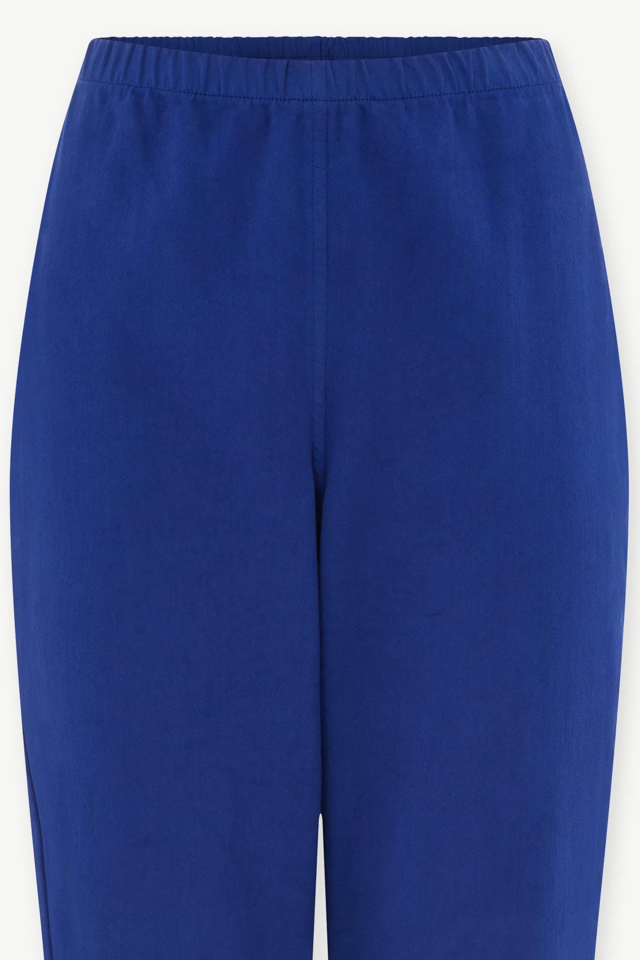 Close-up of SS22 Stretch Cotton Trouser in blue with slim, tapered legs and an elasticated waist, shown front view on a white background. Made from OEKO-TEX certified cotton for comfort and sustainability.