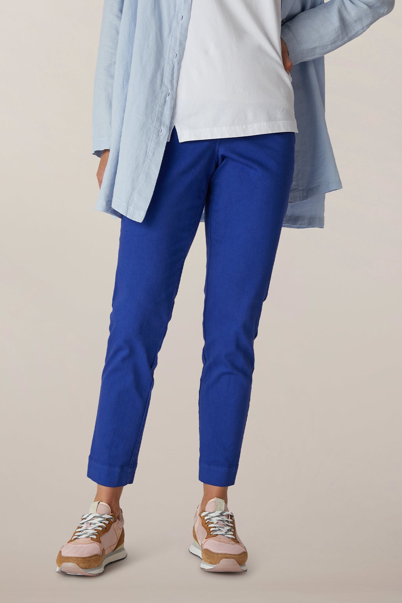 Person wears a light blue shirt, white top, and SS22 Stretch Cotton Trouser in bright blue OEKO-TEX cotton with an elasticated waist, paired with beige sneakers against a neutral background.