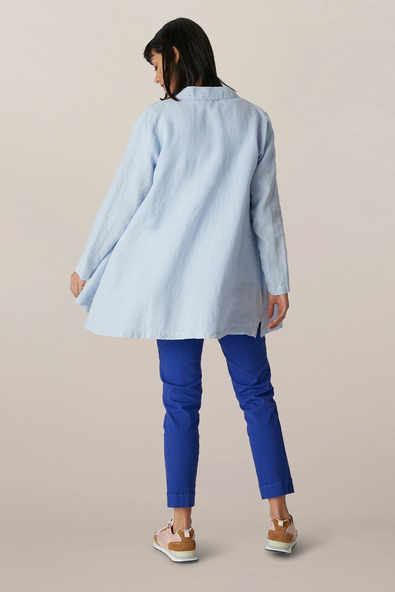 A person stands facing away, wearing a light blue long-sleeve shirt with SS22 Stretch Cotton Trouser in cobalt blue OEKO-TEX cotton and light sneakers, set against a neutral background.