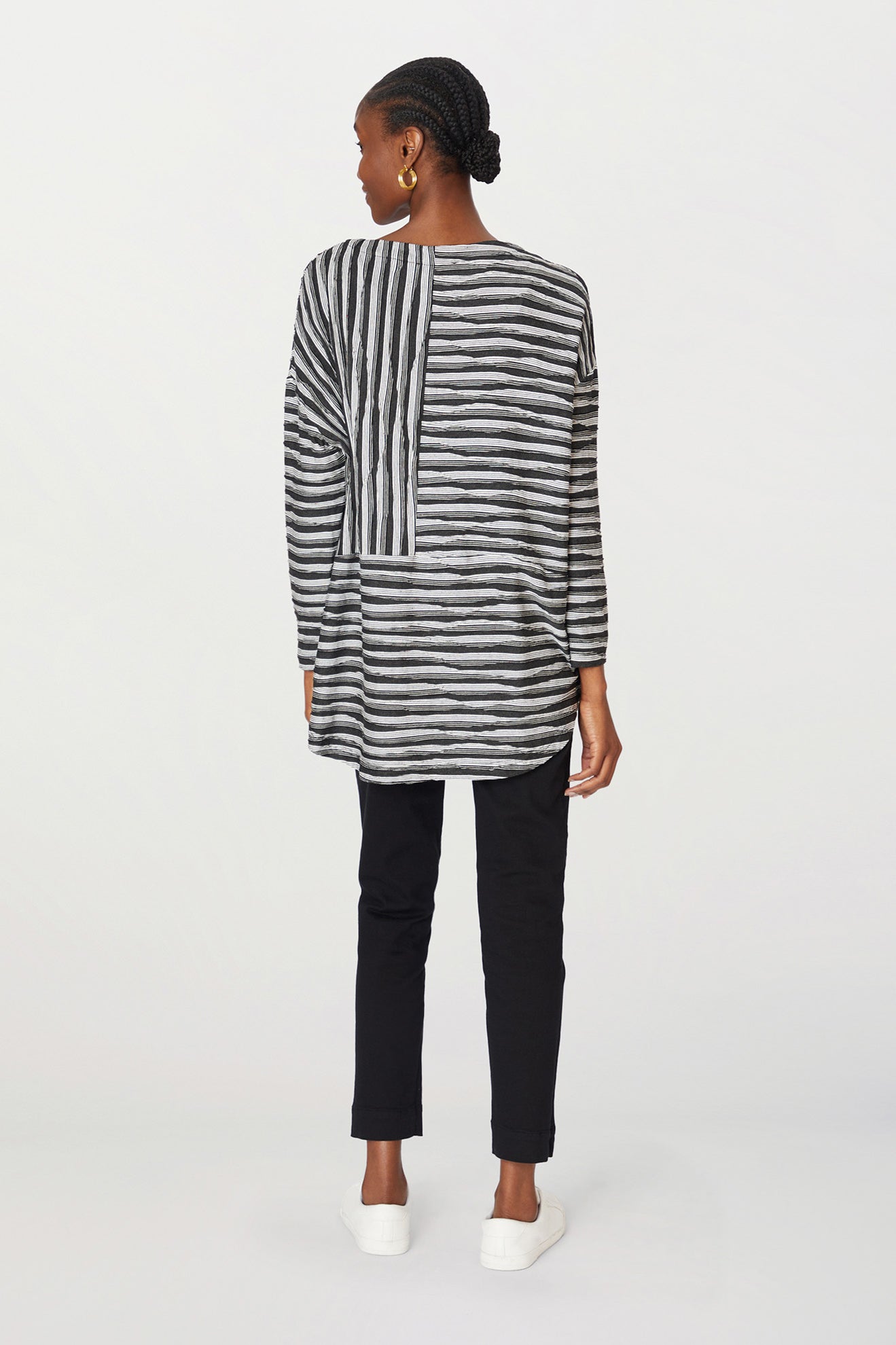 A black woman viewed from the back, wearing a striped shirt and Stretch Twill Cotton Trouser, standing in a neutral pose against a plain background.