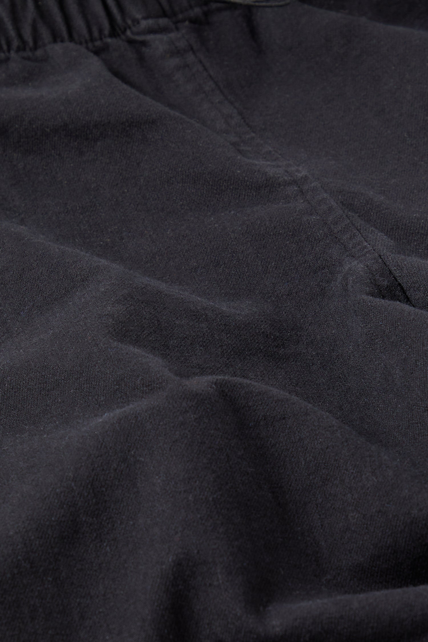 Close-up of black Stretch Twill Cotton Trousers, possibly part of a minimalist wardrobe with visible seams and folds.