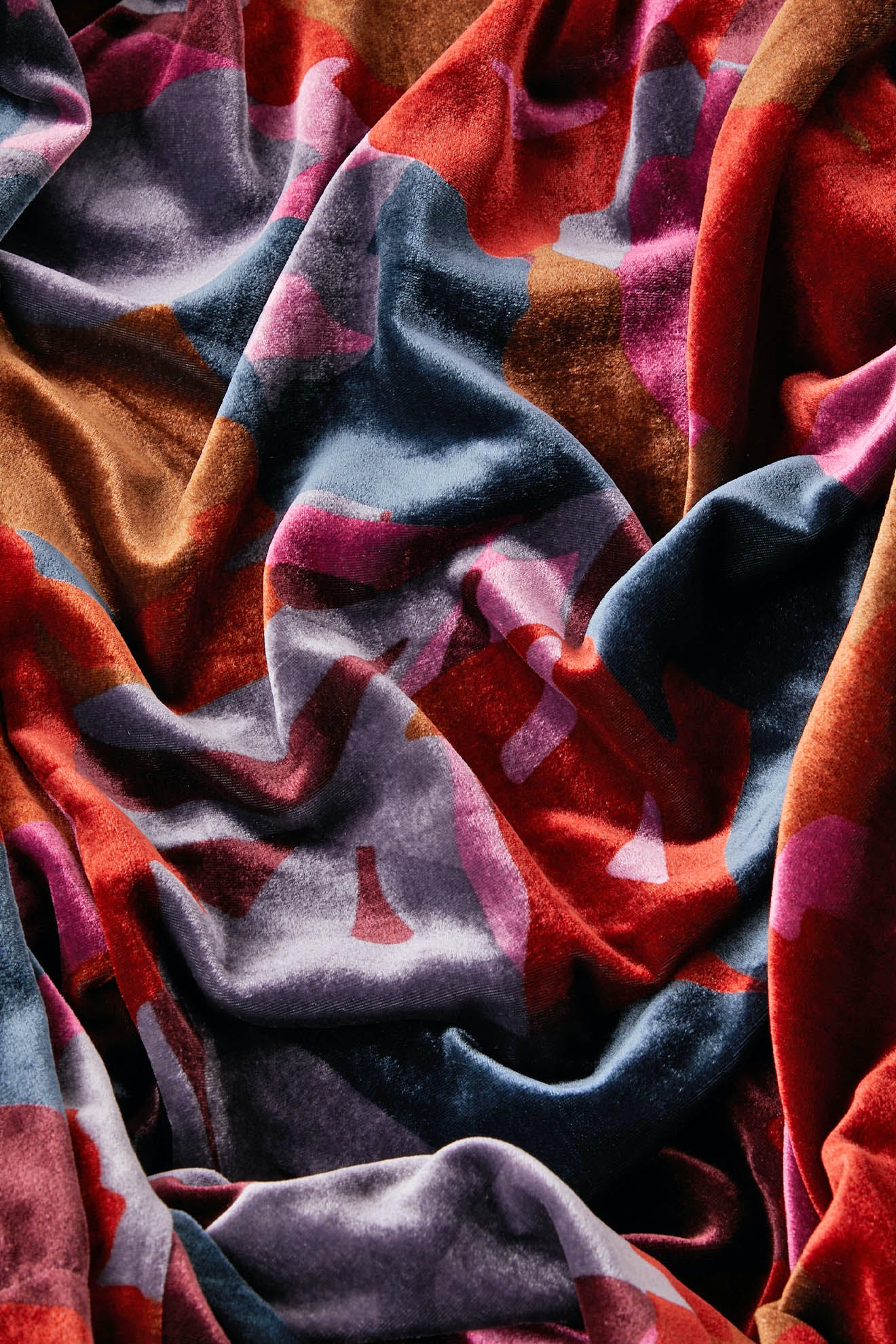 A close-up of the crumpled, multi-colored velvet fabric from the Winter Garden Velvet Top showcases an abstract, wavy pattern with shades of blue, red, purple, and brown—perfect for a decadent evening ensemble.