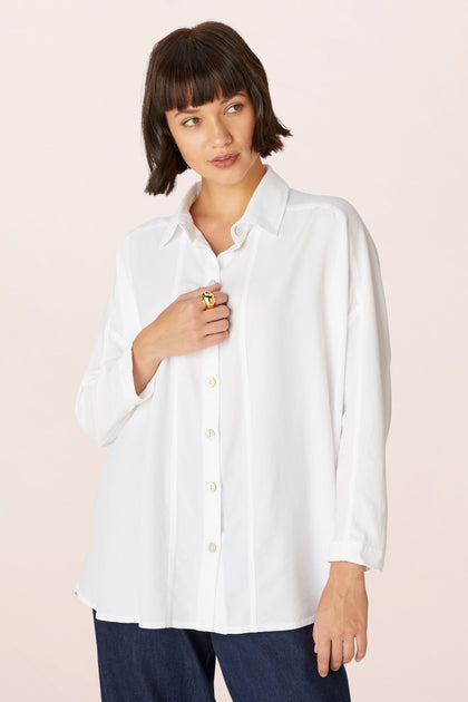A woman with a short bob wears the Tencel Twill Boxy Shirt in white and dark jeans, standing against a plain light background.