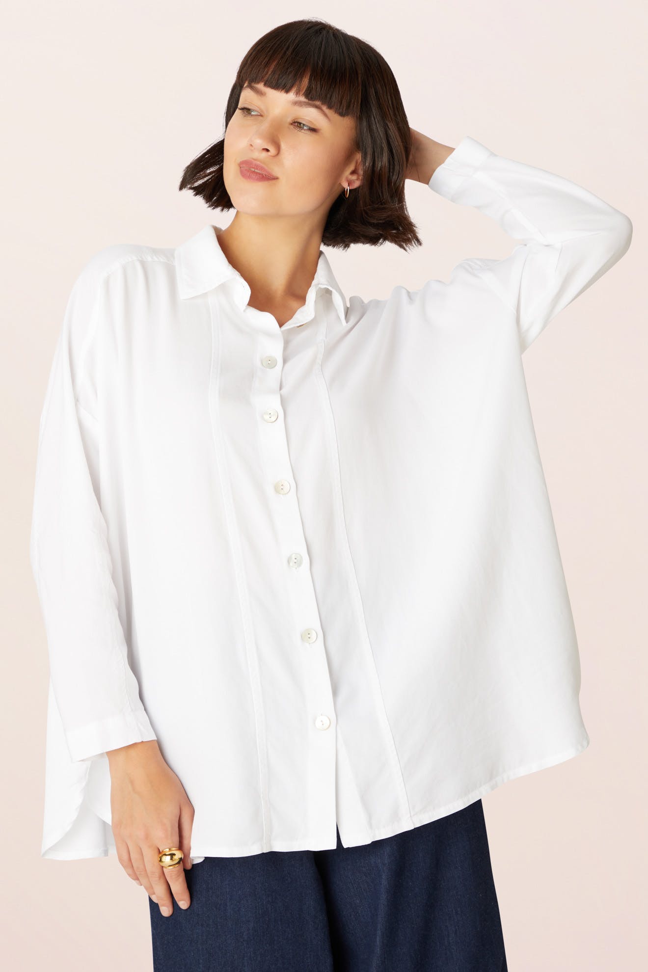 Someone wears the Tencel Twill Boxy Shirt, a loose-fitting white long-sleeve top, paired with dark pants against a light background.