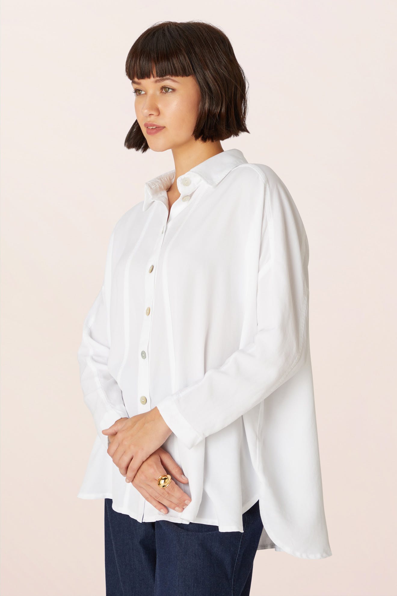 A woman with a bob haircut wears the loose-fitting Tencel Twill Boxy Shirt in white and dark pants, standing against a light background.