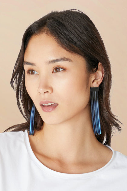 Woman with straight dark hair wearing a white top and Long Fringe Earrings, featuring a blue ombre mesh design, looks slightly to the side against a neutral background.