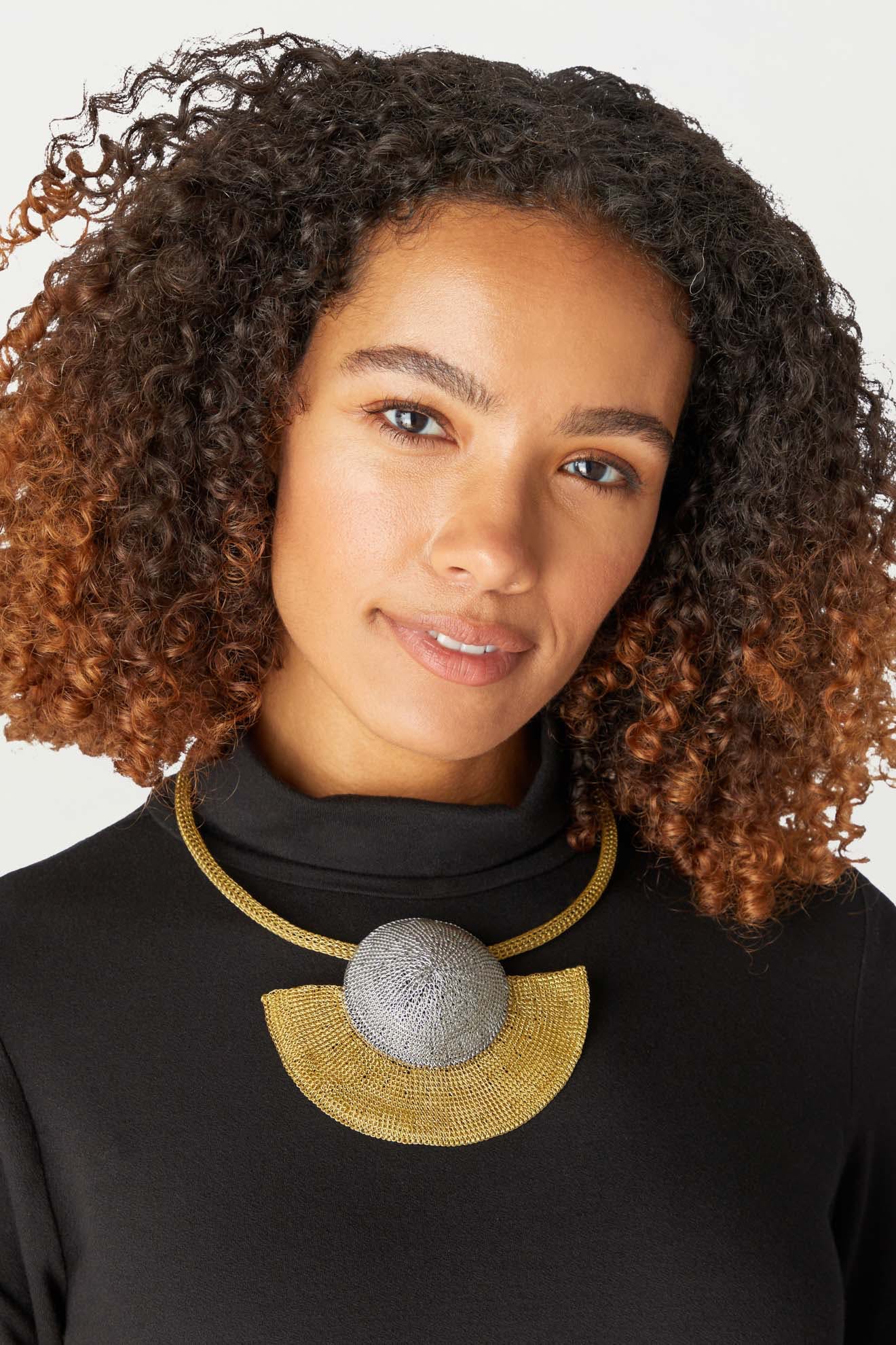 A woman wearing a black top and a gold necklace embellished with the Crochet Half Moon Necklace by Soninké Jewellery.