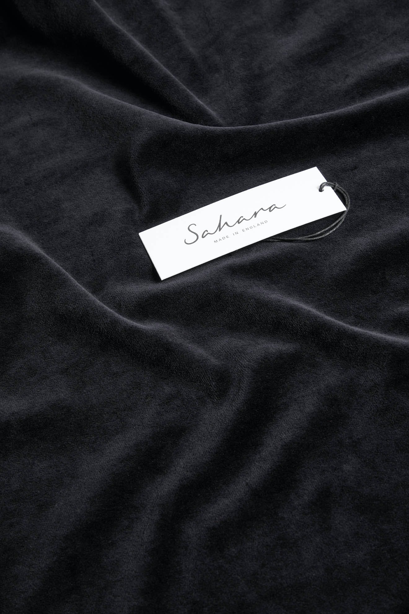 A white tag labeled "Sahara" on a piece of dark, soft fabric, likely the high-quality material of the Velvet Jersey Tube Skirt, with slight folds and creases visible.