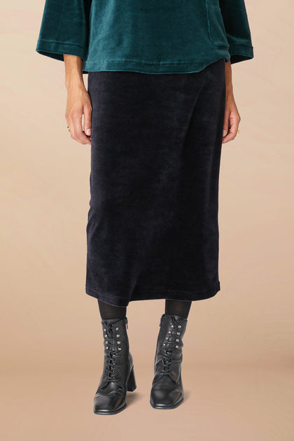 A person wearing a dark green top, the Velvet Jersey Tube Skirt with a classic silhouette, black leggings, and black lace-up boots is standing against a plain background. Only the lower half of the body is visible.