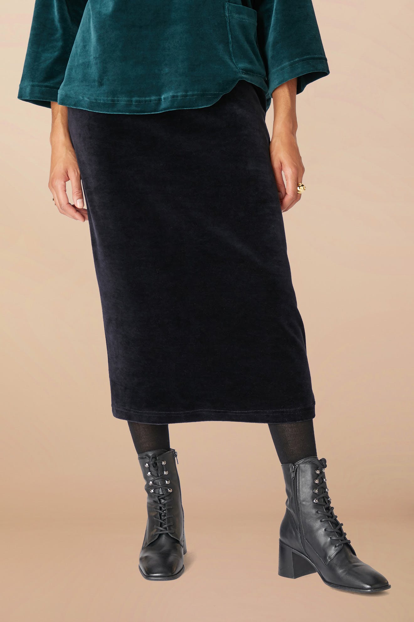 Person wearing a green long-sleeved top, Velvet Jersey Tube Skirt in black, and black lace-up ankle boots, standing against a plain background, showcasing a classic silhouette.