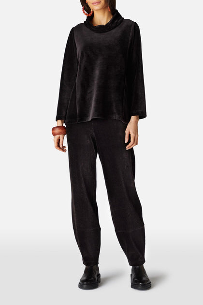 A person wearing the Velvet Rib Jersey Top, velvet jersey slim trousers, black shoes, a red earring, and a wooden bracelet is standing against a plain white background.