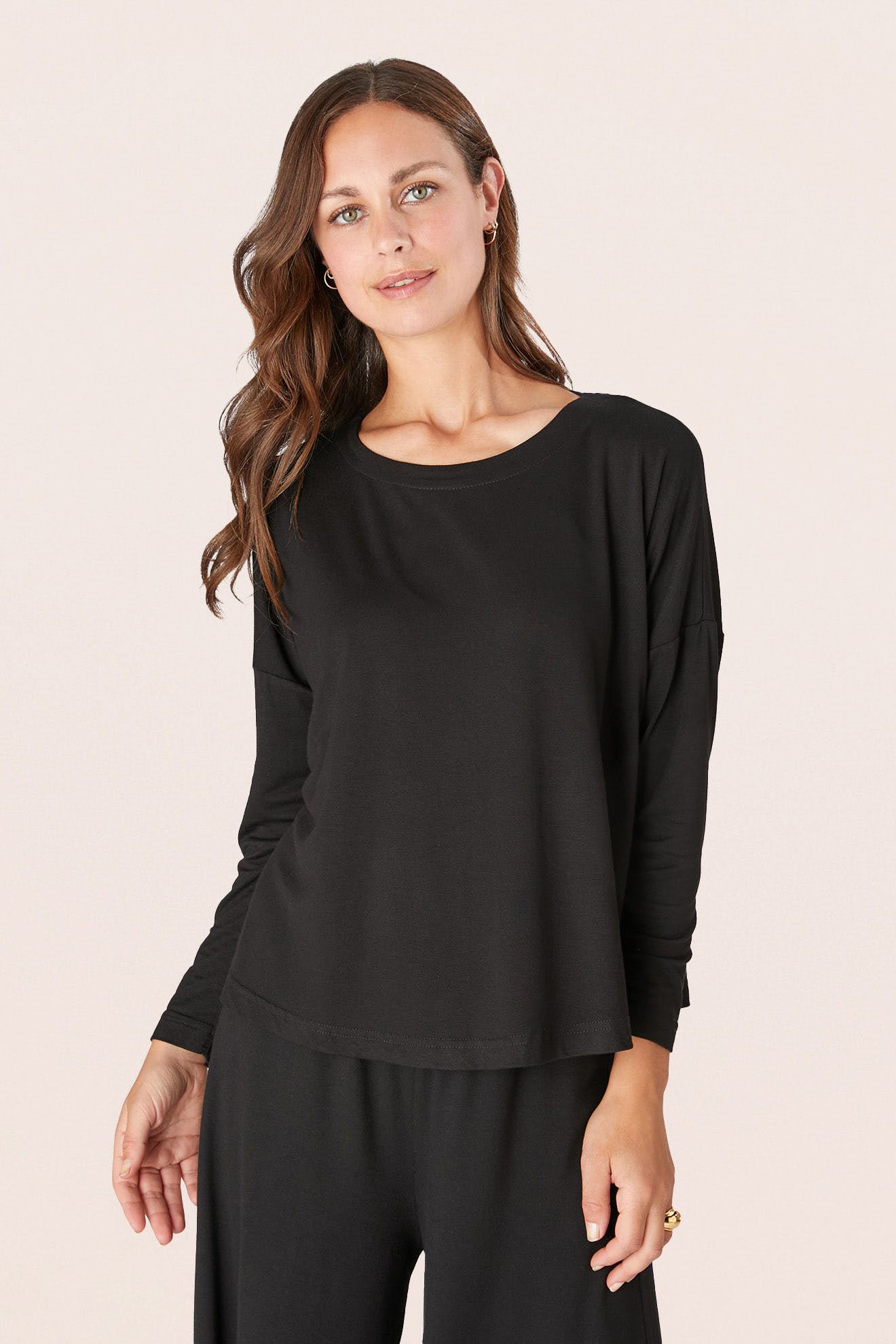A person with long brown hair wears a Fluid Crepe Jersey Relaxed Top in black and matching pants, standing against a plain background.