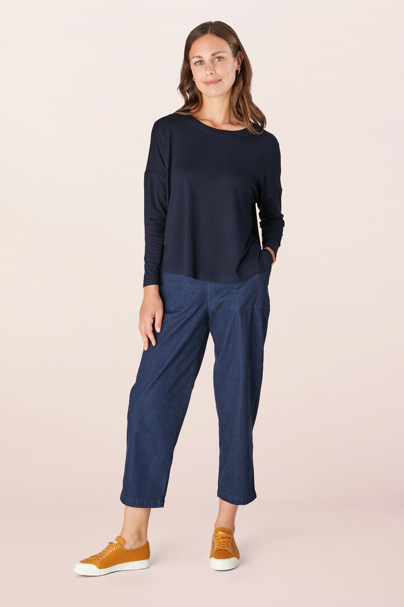 A person wearing a Fluid Crepe Jersey Relaxed Top in navy, blue pants, and orange sneakers stands against a plain background, showcasing a wardrobe hero.