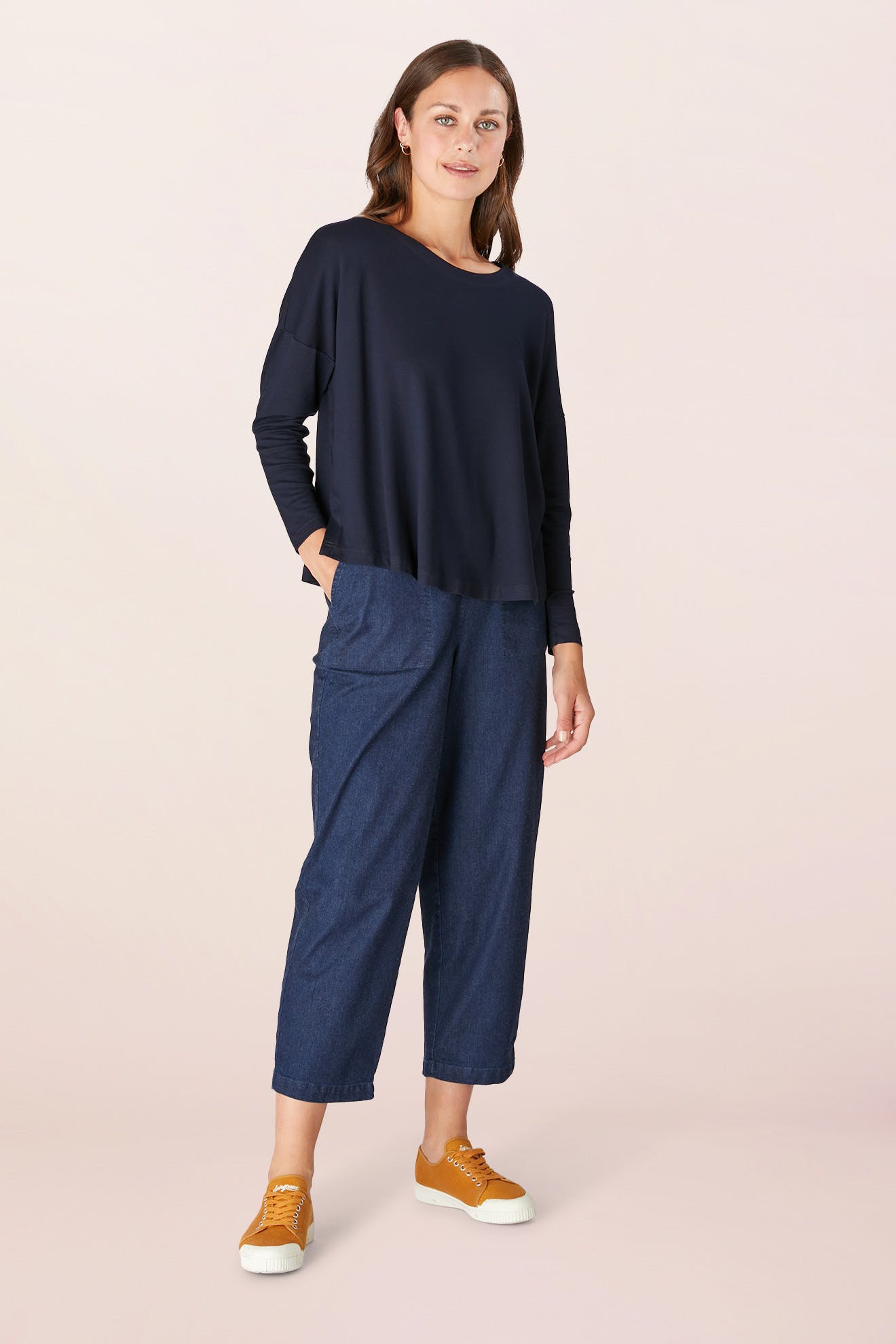 A person in a Fluid Crepe Jersey Relaxed Top, blue pants, and yellow sneakers stands against a plain background, embodying the essence of a true wardrobe hero.