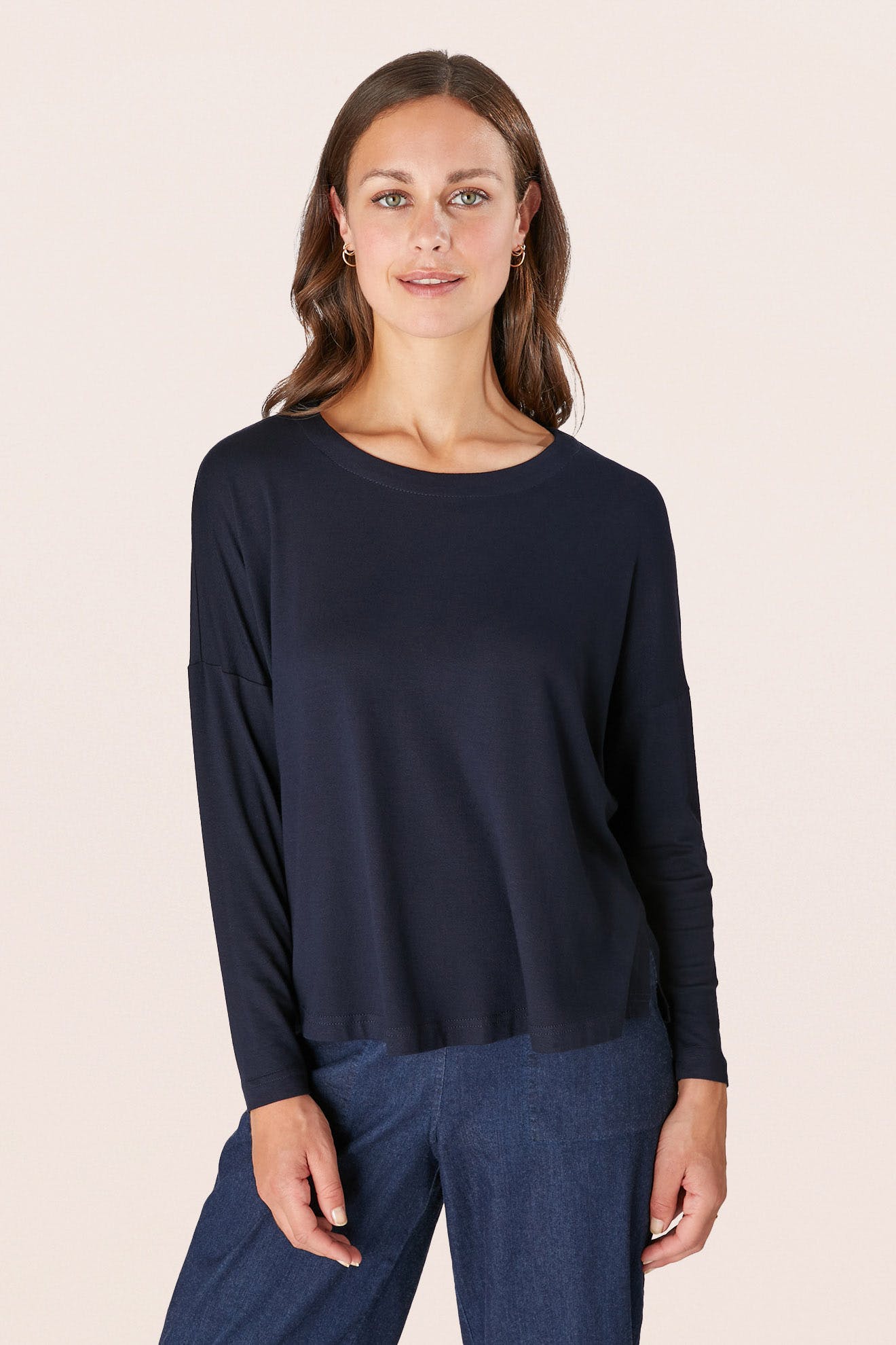 A person with long hair is wearing a navy Fluid Crepe Jersey Relaxed Top and denim pants, standing against a plain background.