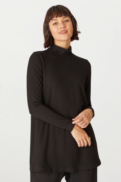 A woman with short brown hair wears the Fluid Crepe Flared Polo Neck and black pants, standing against a plain white background.