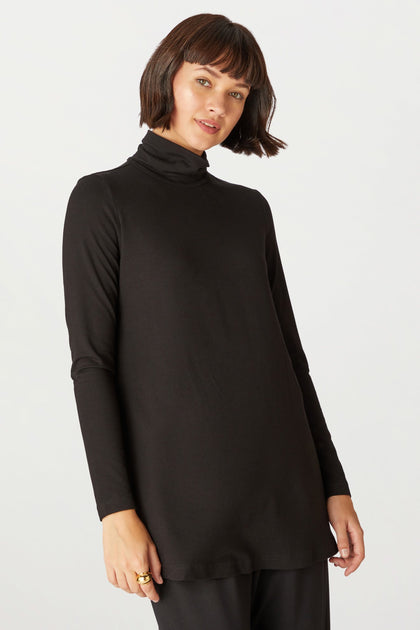 A woman with short brown hair wears the Fluid Crepe Flared Polo Neck and black pants, standing against a plain light background.