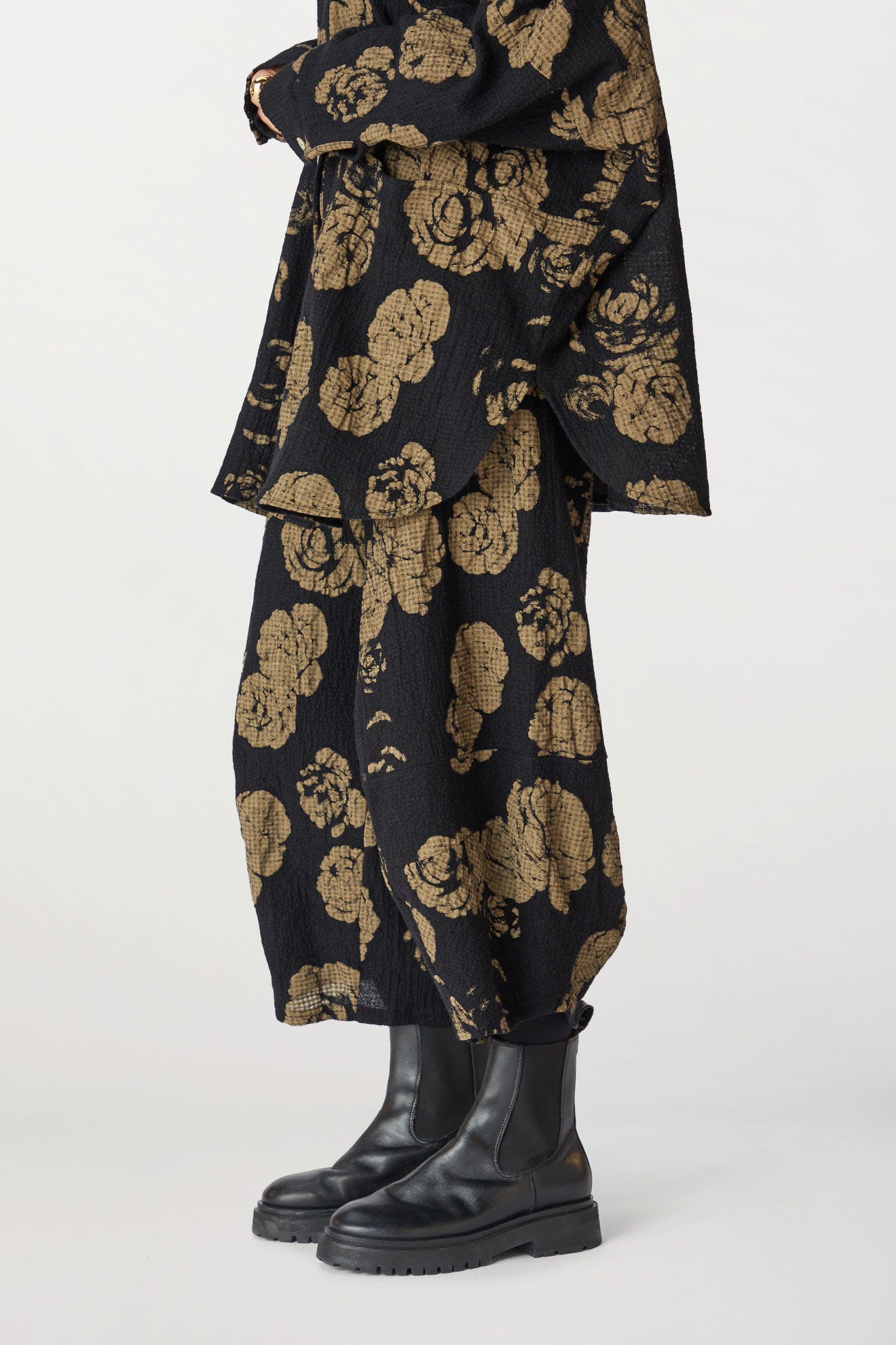 A person wearing a dark rose print pant with chunky black boots, standing against a plain white background.