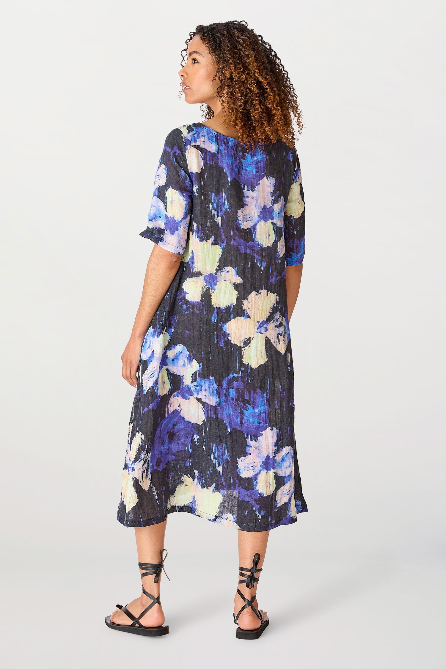 Woman in a Floral Linen Dress looking over her shoulder, standing against a plain background.
