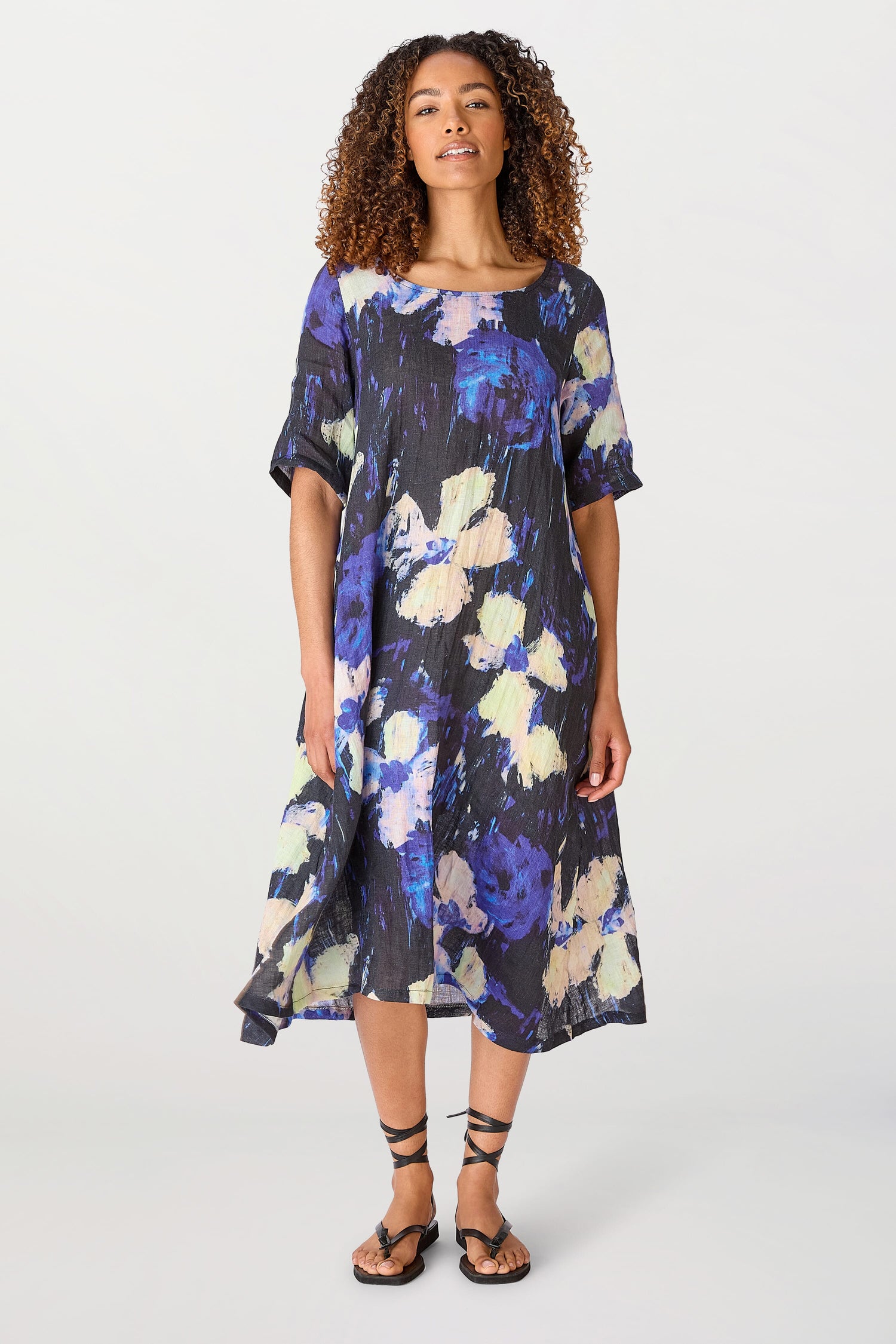 A woman in a Blue and Yellow Floral Linen Dress standing against a white background, wearing black strappy sandals.