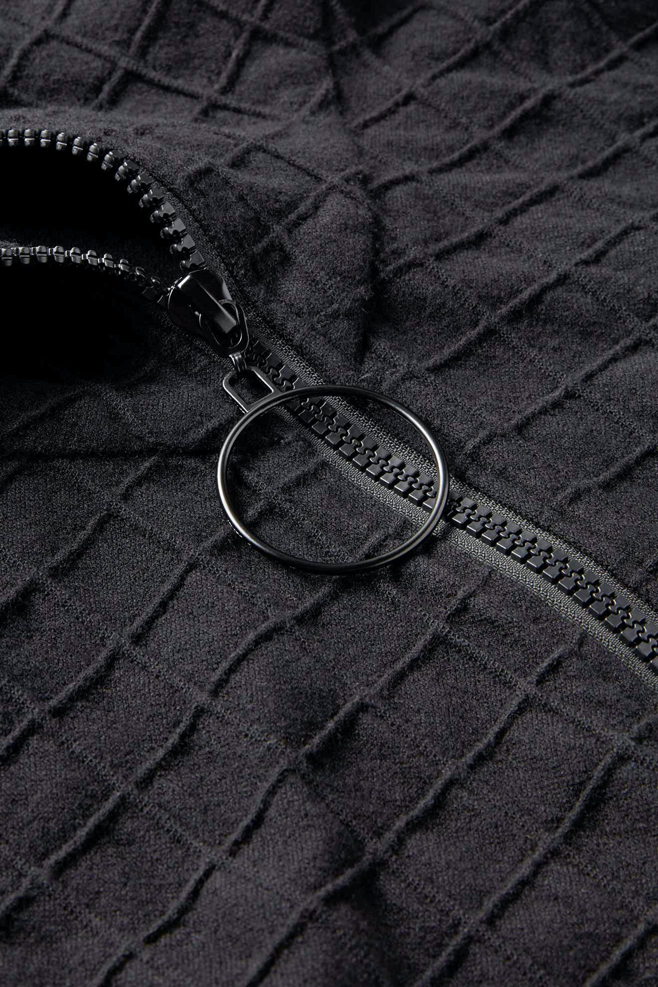 Close-up of a black textured fabric with a half-opened zipper and a circular pull tab, reminiscent of the refined design found in the Window Pane Wool Jacket.