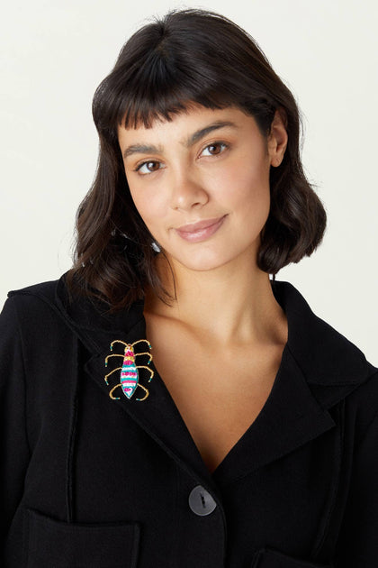 A person with short dark hair wearing a black blazer adorned with the Sequin Detail Brooch on the lapel, showcasing intricate embroidery and vibrant seed beads.