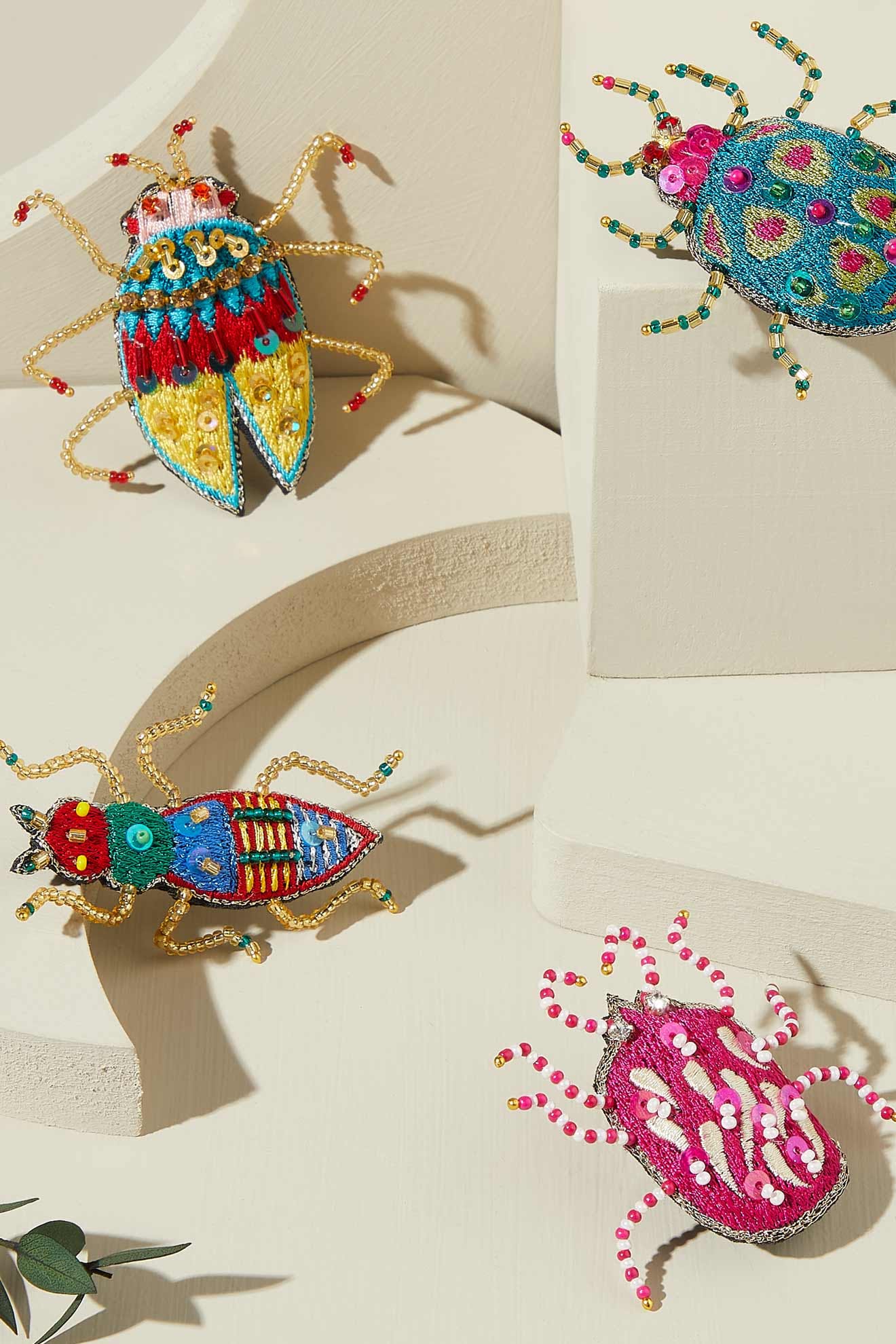 A Pink Detail Beetle Brooch with intricate patterns and vibrant hues is displayed on a cream-colored geometric platform.