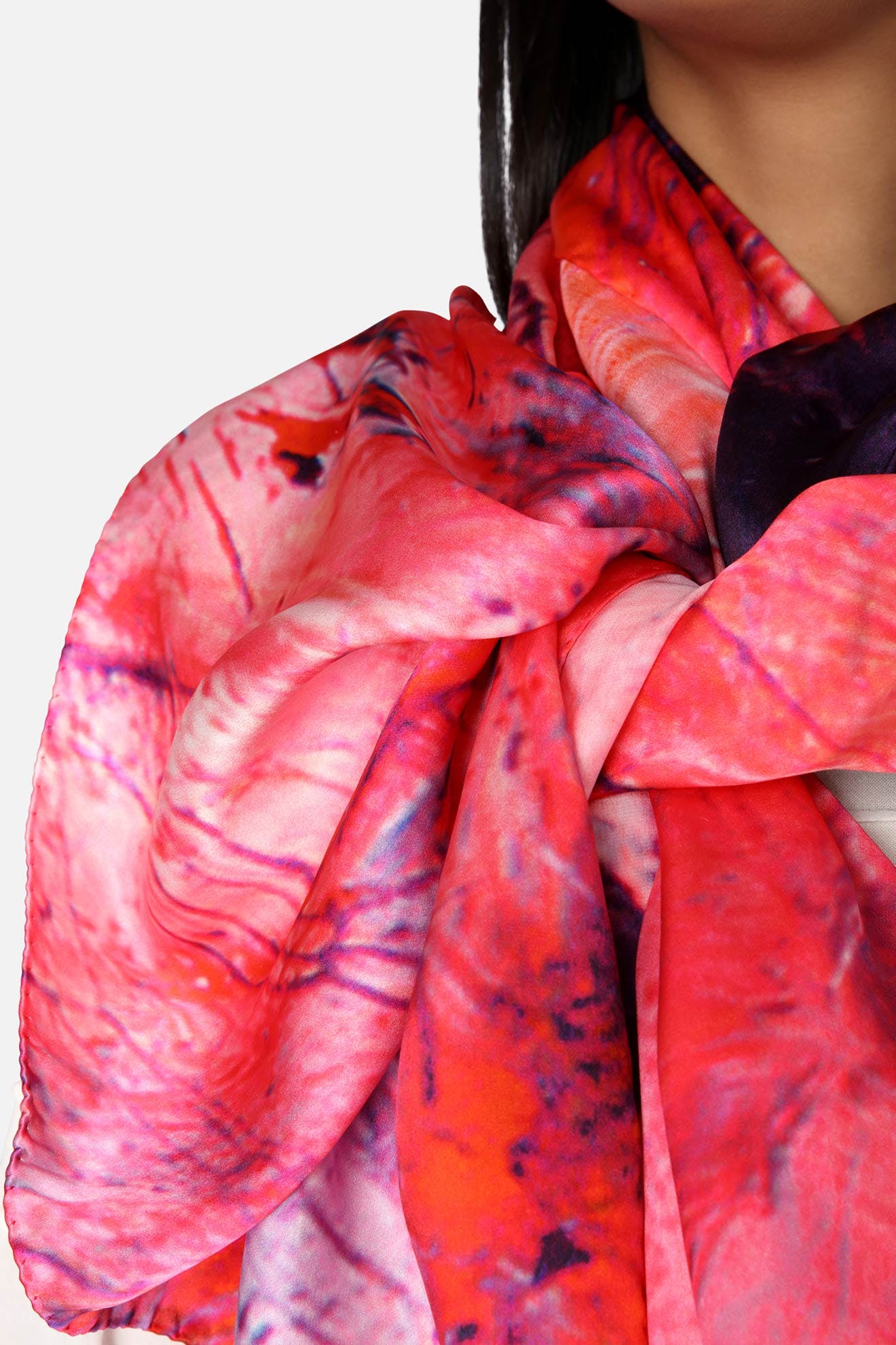 Close-up of a person wearing the Heavenly Calcite Scarf, a vibrant, multicolored silk accessory featuring shades of pink, red, and purple. Only the lower face and neck of the person are partially visible, showcasing the fashionable scarf in vivid detail.